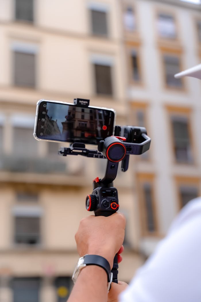 A person uses a smartphone on a gimbal to film an urban setting.